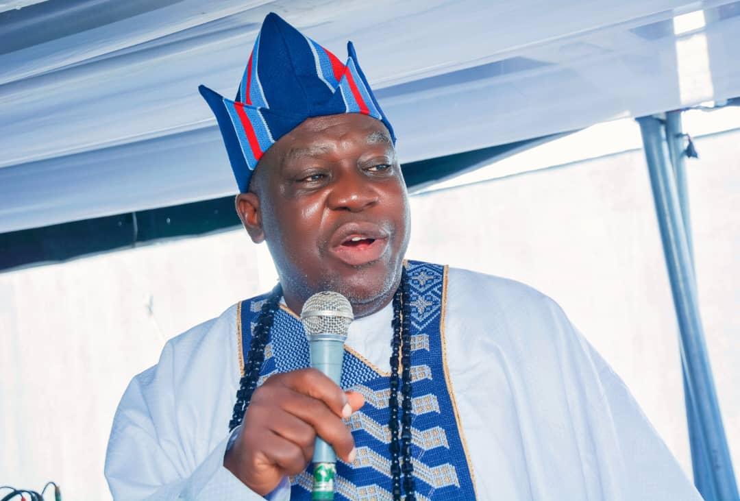 A speaker in a beaded cap addressing the New Yam celebration with a microphone